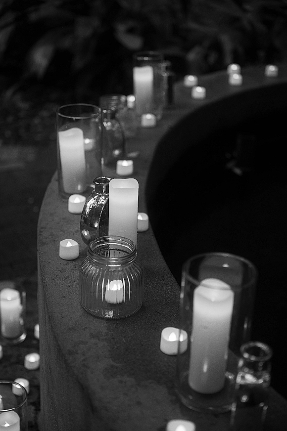 Wedding candle decor lining a candlelit wedding aisle with pillar and tea light candles in glass hurricane vases, set in a dark room with greenery
