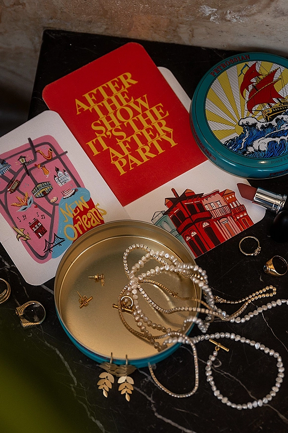 Bridal jewelry flatlay with wedding rings flatlay, pearl necklace, rhinestone bracelet, earrings and cards arranged on marble beside a black clutch