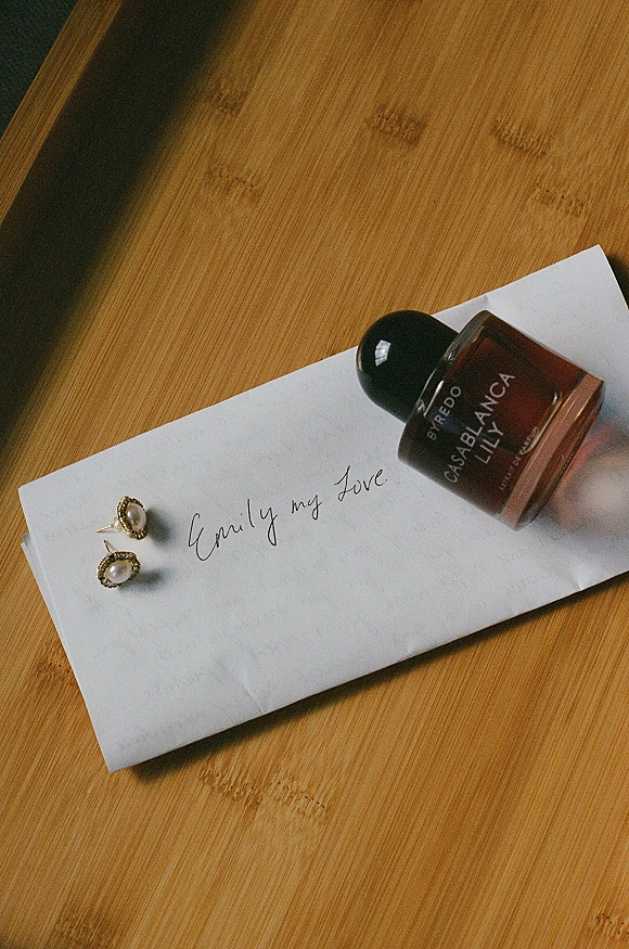 Love letter and handwritten love note on a wooden tabletop with envelope, pearl earrings, and perfume bottle in soft window light