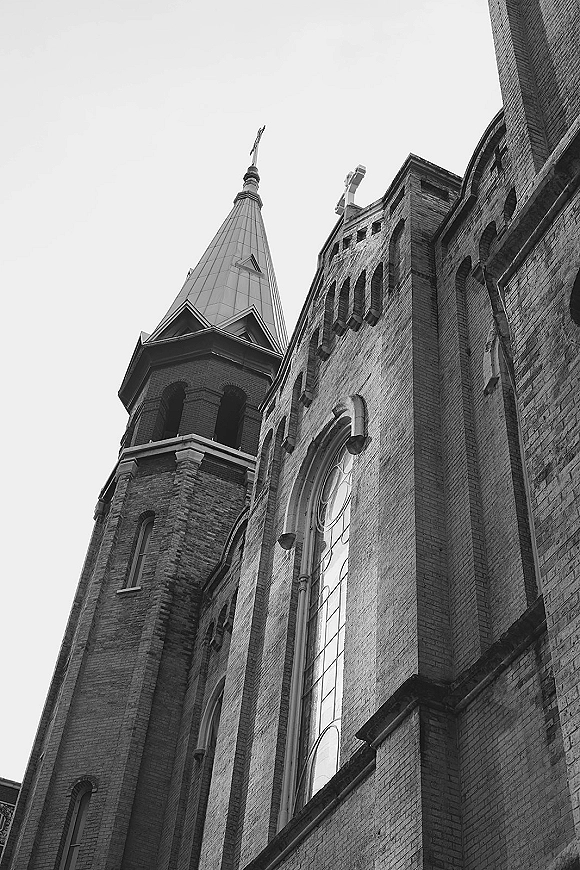 Church exterior with brick facade and steeple topped by a cross, arched windows rising against the open sky overhead