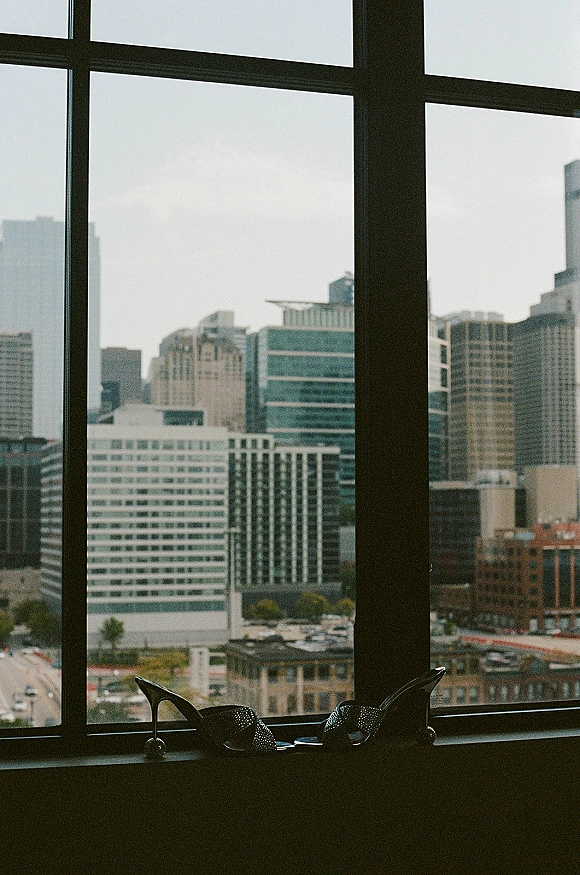 Bridal shoes and wedding heels with sparkly high heels on a windowsill by a large window, city skyline visible in the background