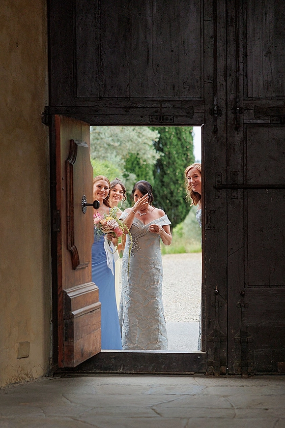 Bridesmaid entrance with bridesmaids entering ceremony in blue dresses, holding bouquets with ribbon by rustic wooden doors and greenery backdrop