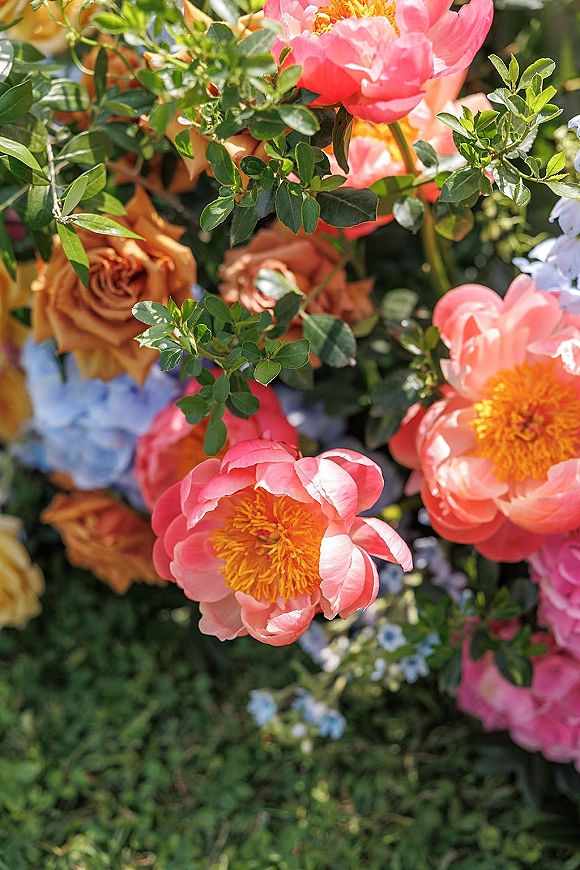 Bridal bouquet with coral peonies and peach roses, blue hydrangea and lush greenery, hand-tied over garden grass backdrop