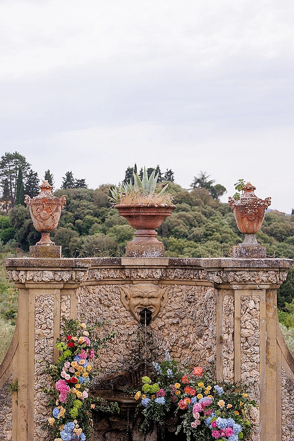 Wedding floral installation with fountain floral installation of roses, hydrangeas, and greenery cascading over a stone garden fountain wall