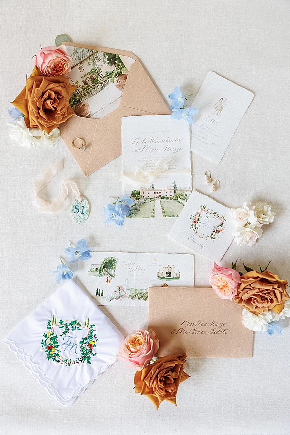 Wedding invitation suite with deckle edge wedding invitations, silk ribbon, wax seal, rings, and blue florals on white linen flat lay