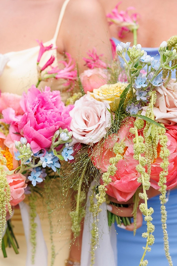 Bridal bouquet with colorful wedding bouquet roses in pink and blue, a yellow rose, trailing greenery and ribbon resting on the bride’s lap