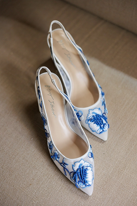 Bridal shoes with blue floral wedding shoes embroidery, pointed toe slingback heels with sheer mesh panels resting on a beige chair