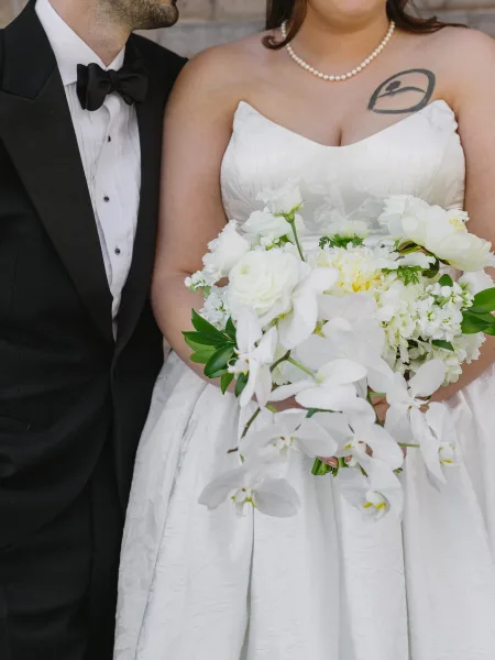 Bridal bouquet, a phalaenopsis orchid bouquet with airy greenery, held close against a rustic stone wall backdrop.