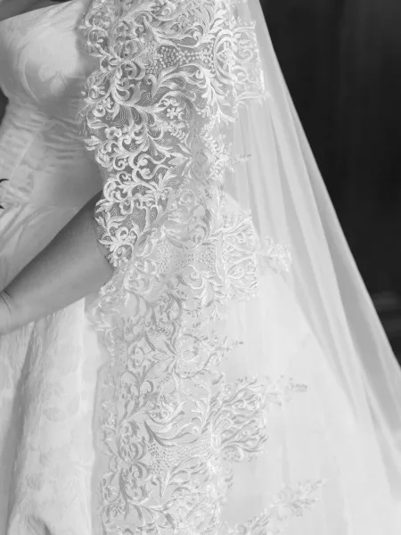 Bridal veil detail shows a lace edge veil with fine lace applique, its sheer layers falling gracefully against a dark wall.