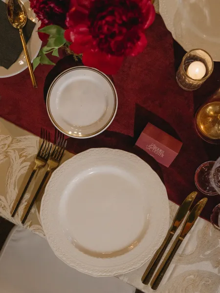 Wedding place setting on a burgundy and gold wedding table, highlighted by gold flatware on a damask tablecloth.