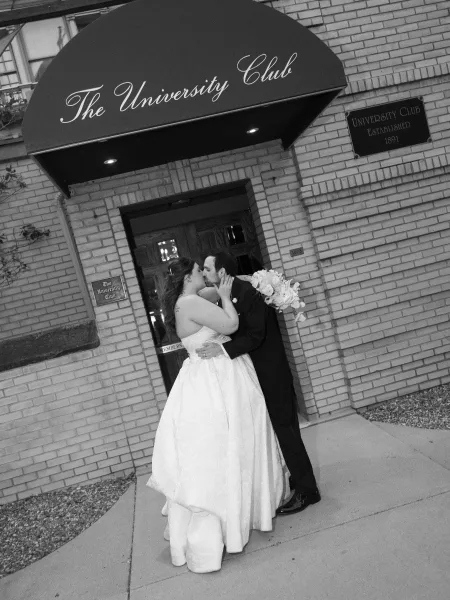Wedding kiss portrait of the couple sharing a doorway wedding kiss under an awning at a brick venue, the bride holding a bridal bouquet.
