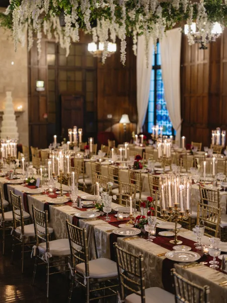 Reception tablescape glowing in a candlelit wedding reception, centered with candelabras before a stained glass window backdrop.