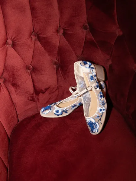 Bridal shoes with blue embroidery, elegant blue wedding shoes resting on a burgundy tufted velvet chair.