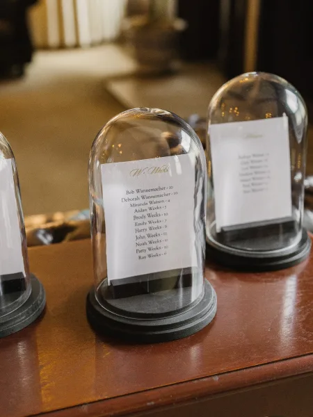 Escort card display with glass cloche escort cards arranged in tidy rows atop a wood tabletop, creating a refined focal point.