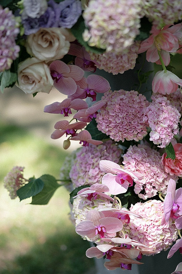 Wedding floral arrangement with hydrangea wedding flowers, roses and orchids, overflowing with greenery against a softly blurred garden backdrop