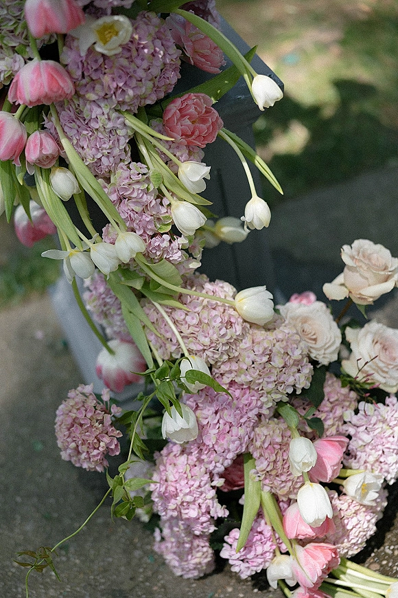 Wedding floral arrangement of pink and white tulips, hydrangeas, and roses with greenery on a black pedestal by stone steps outdoors
