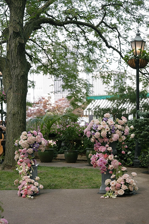 Wedding ceremony florals and floral ceremony pillars with pastel roses, hydrangeas, orchids, and tulips on pedestals along a garden walkway