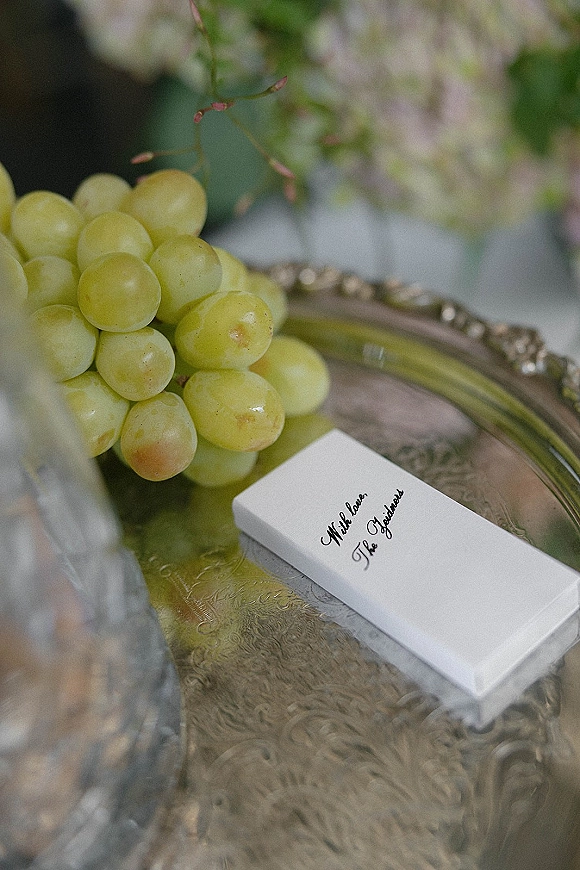 Wedding favor box with personalized wedding favors calligraphy label on a silver tray, nestled with green grapes and greenery against soft florals