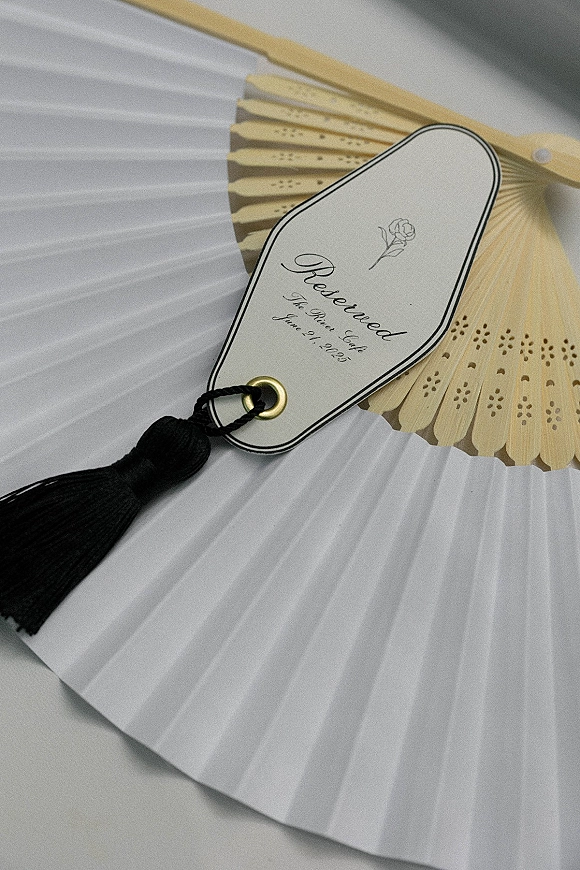 Reserved seat sign on a paper hand fan with wooden ribs, calligraphy tag, black tassel, and gold grommet on white fan surface