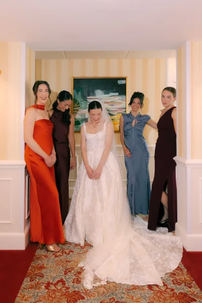 Bride with bridesmaids in a bridal party portrait, her long veil and lace train flowing in a classic hotel hallway with striped wallpaper