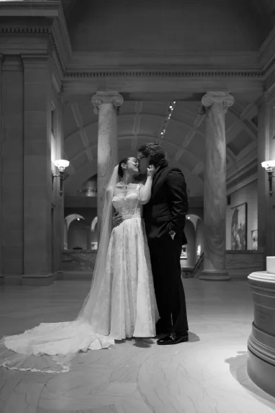 Wedding kiss portrait in black and white of bride and groom kissing, her long veil flowing in a grand marble hallway with columns and arches