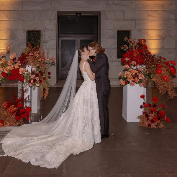 Wedding kiss portrait of bride and groom kissing, her cathedral veil and lace train flowing in a marble entryway with floral plinths