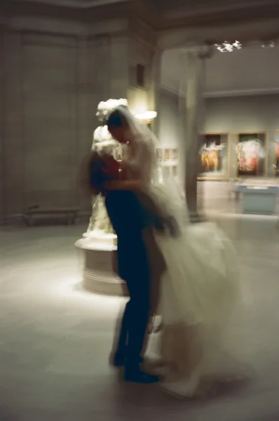 Wedding kiss portrait of bride and groom kissing, her long bridal veil sweeping behind in a museum gallery with framed artwork and columns