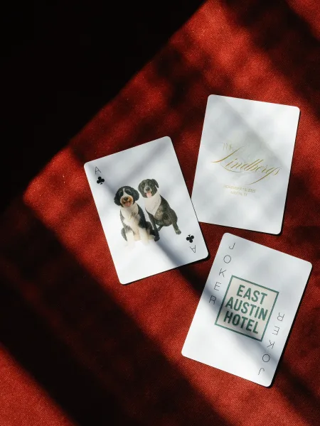 Invitation suite wedding stationery flat lay with gold foil lettering and playing cards on red fabric, with soft window-light shadows