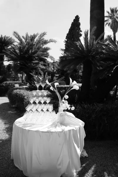 Champagne tower setup with coupe glass champagne tower stacked on a white linen round table, calla lily centerpiece, palm garden backdrop