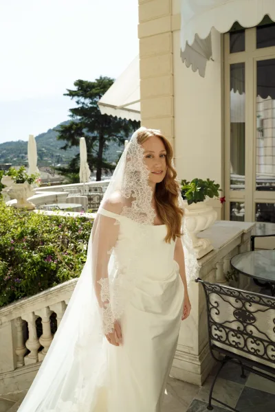 Bridal portrait of a bride in a lace veil and off the shoulder gown on an outdoor terrace with stone balustrade and mountains beyond