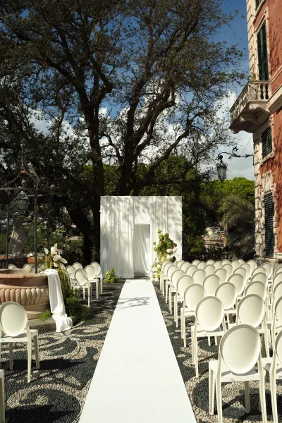 Ceremony setup for an outdoor wedding ceremony with white aisle runner, chairs, and draped backdrop on a stone terrace overlooking hills
