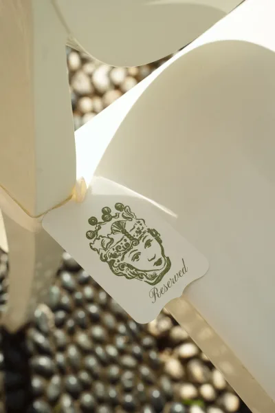 Reserved seat sign tied with a ribbon to a ceremony chair, reserved tag resting on the chair back in warm sunlight on pebbles