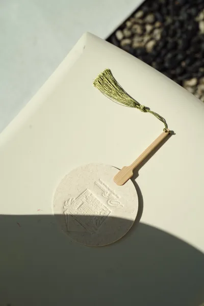 Wedding invitation with embossed wedding invitation details on deckle edge paper, finished with a gold tassel on a white surface beside dark stone