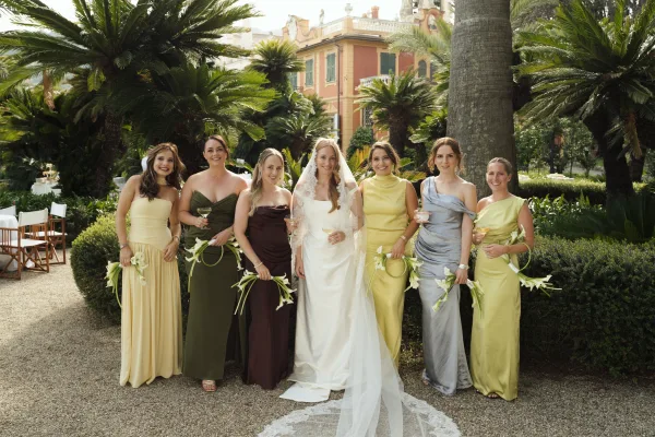 Bridesmaid group photo with bride with bridesmaids holding calla lily bouquets and champagne glasses on a gravel path by palm trees