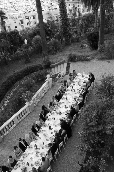 Wedding reception dinner with a long banquet table, white tablecloth and taper candles on an outdoor terrace overlooking a marina view