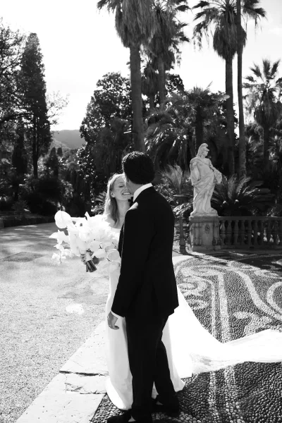 Couple portrait in black and white wedding portrait style, bride smiling at groom holding a calla lily bouquet on a mosaic terrace with palms
