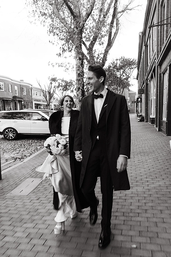 Wedding couple portrait in a black and white wedding photo, bride and groom walking hand in hand on a city sidewalk with brick buildings behind