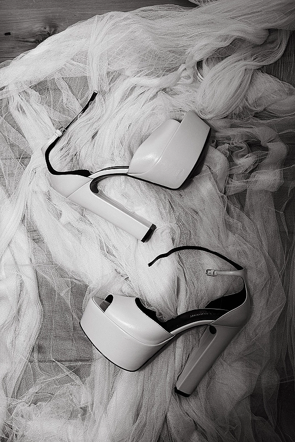 Bridal shoes in white wedding heels style, strappy platform sandals with ankle straps on a wood floor beside soft tulle fabric