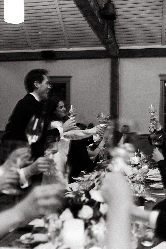 Wedding toast as bride and groom raise champagne flutes over a candlelit banquet table in a reception hall with rustic wooden beams