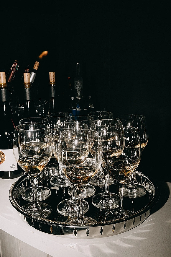 Champagne service tray with wedding champagne glasses, bottles, and a silver tray on a white tablecloth at a dark bar setup