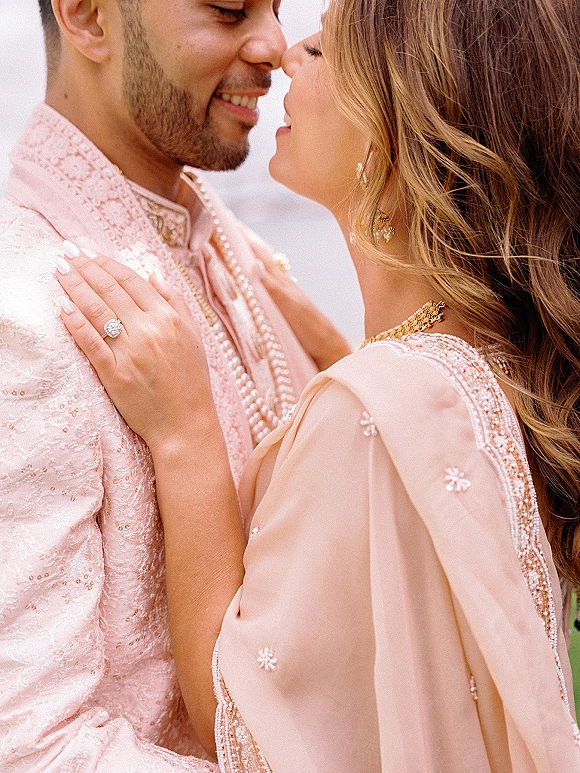 Wedding couple portrait of a South Asian bride and groom forehead to forehead, her hand on his beaded sherwani, ring visible on neutral backdrop