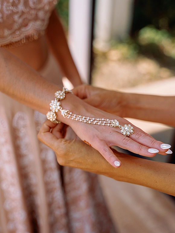 Bridal jewelry wedding hand chain sparkling with rhinestones across manicured fingers against a lace wedding dress and soft greenery doorway backdrop