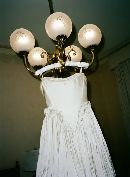 Wedding dress hanging from a chandelier, a strapless wedding dress with fitted bodice, gathered skirt, and ruffle trim in a curtained room