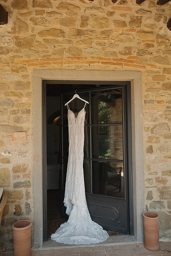 Wedding dress, lace wedding dress on a hanger with spaghetti straps and V-neckline, hanging in a stone doorway with terracotta pots