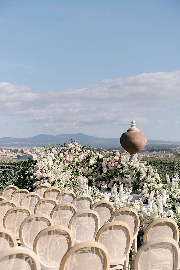 Ceremony setup with floral altar arrangement of white and blush flowers, greenery, and aisle blooms on a terrace with mountain view