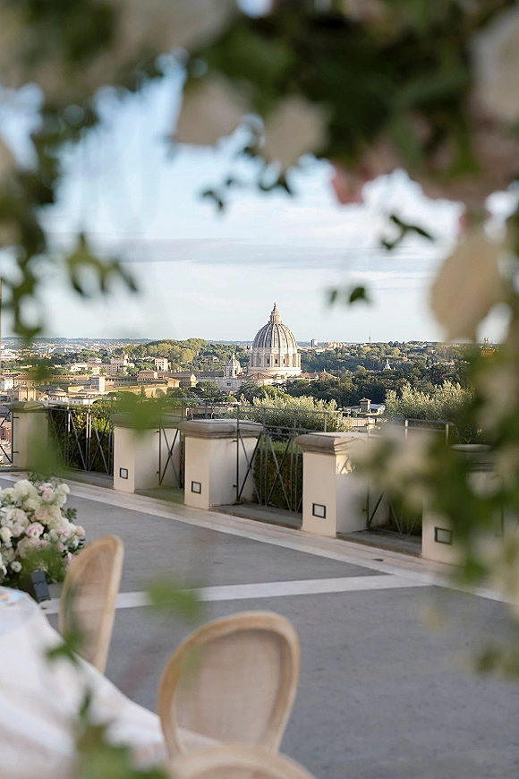Reception terrace view with wedding terrace reception tables, white tablecloths and floral centerpieces, overlooking a city skyline and dome building