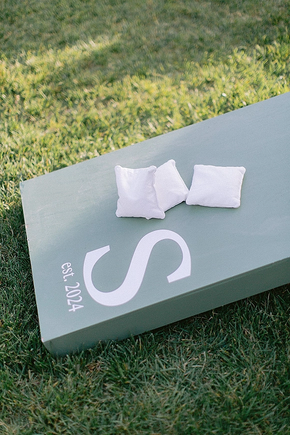 Wedding cornhole set with custom cornhole boards and bean bags, featuring a painted monogram and wedding date on a grass lawn