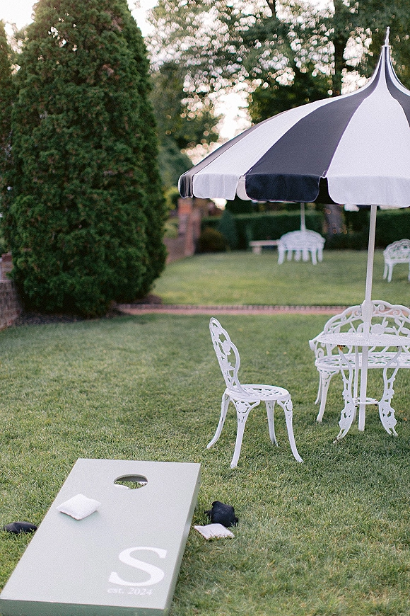 Wedding lawn games with wedding cornhole boards and bean bags beside a patio umbrella and bistro table on a grassy garden lawn