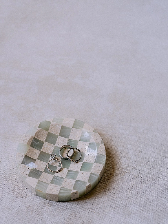 Wedding rings and engagement ring close up stacked in a checkered stone dish on a soft linen fabric surface
