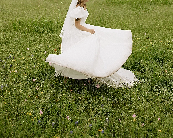 Bridal portrait of a bride twirling her wedding dress, long train flowing with a veil in a wildflower meadow grass field